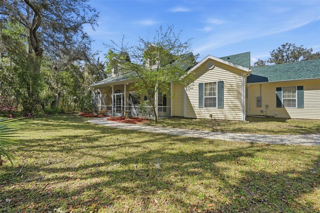 A yellow house with green shingled roofs and a screened-in porch sits on a lawn — 35015 RADIO ROAD, LEESBURG, FL