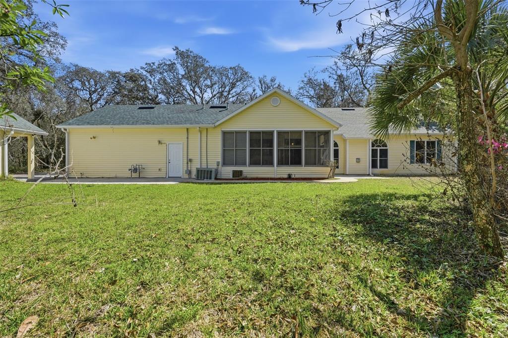 The exterior rear view of a yellow house features a screened-in porch and grassy yard — 35015 RADIO ROAD, LEESBURG, FL
