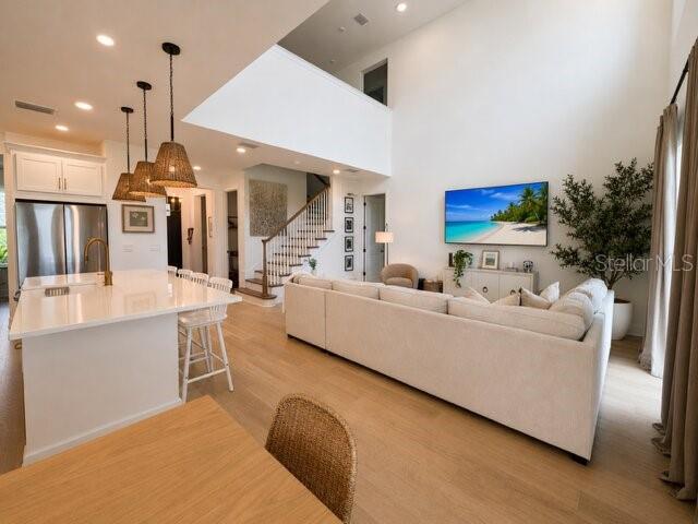A bright, open-concept living room and kitchen featuring light wood floors and high ceilings — 8532 GOLDEN DAWN COURT, SARASOTA, FL