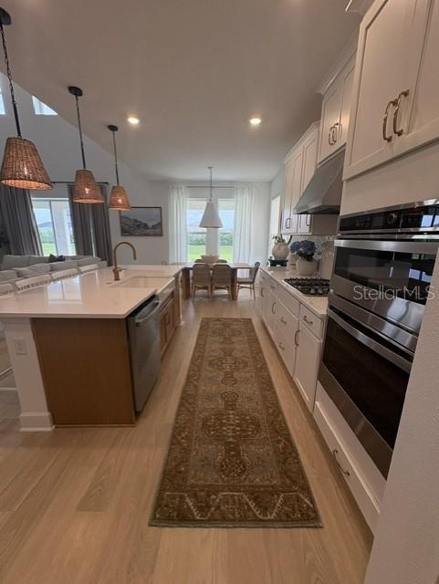 A modern kitchen features white cabinetry, a large island with pendant lights, and wood flooring — 8532 GOLDEN DAWN COURT, SARASOTA, FL
