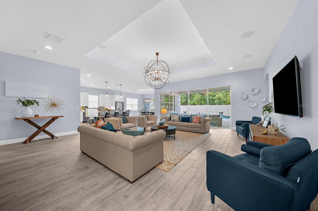 A spacious open-concept living room features a tray ceiling, tile flooring, and sliding glass doors — 2013 BEE BRANCH COURT, PALM HARBOR, FL
