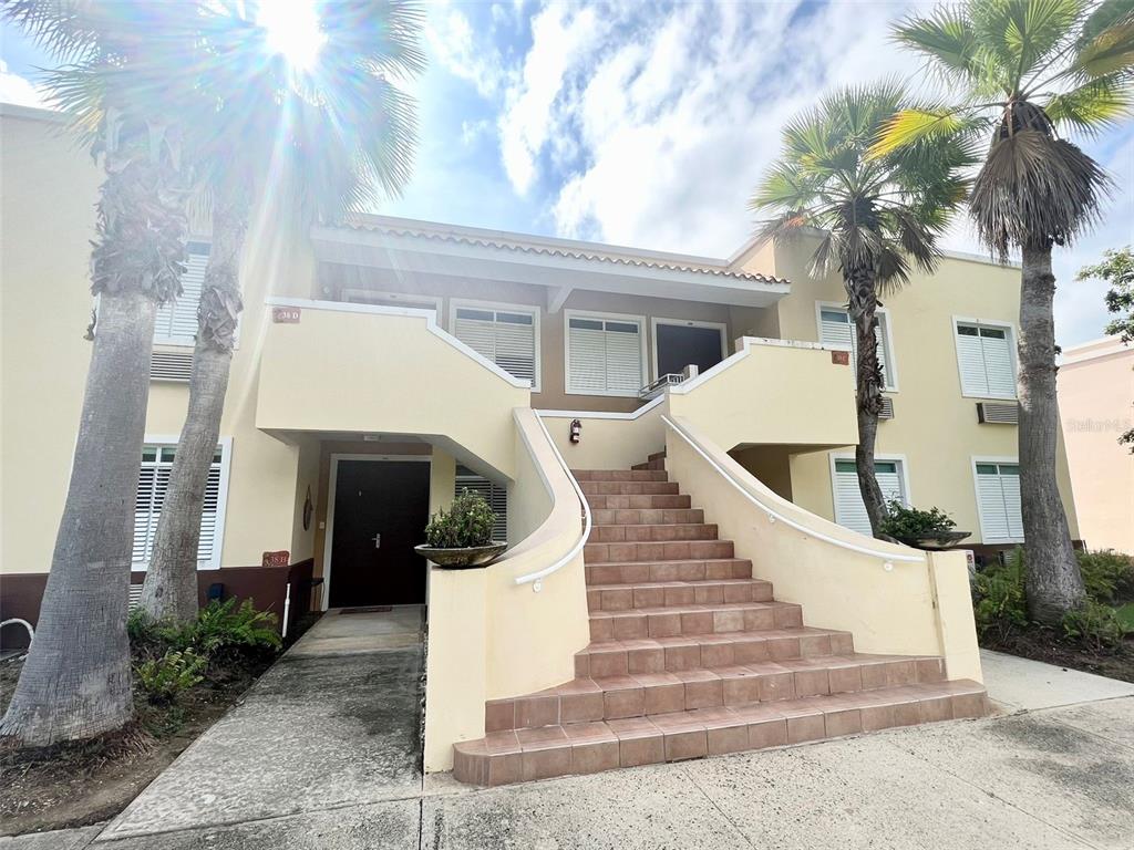 An exterior view of a two-story apartment building with a central staircase and palm trees — 180 PALMAS DRIVE UNIT 38-D, HUMACAO, PR