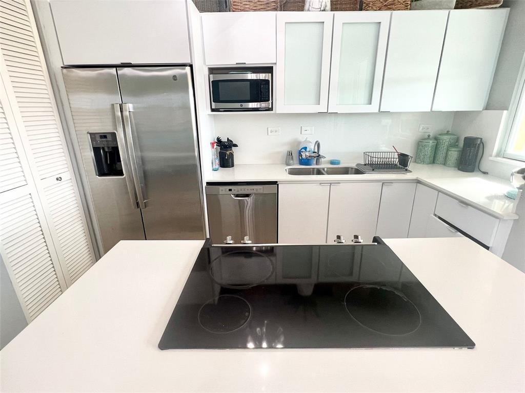 A modern kitchen features white cabinets, stainless steel appliances, and a central island cooktop — 180 PALMAS DRIVE UNIT 38-D, HUMACAO, PR