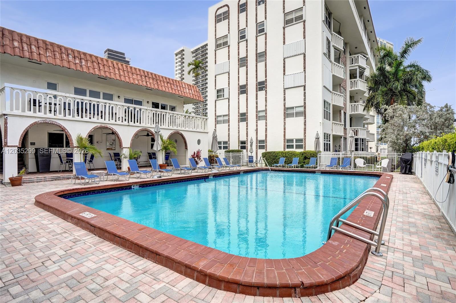 A rectangular swimming pool sits on a brick patio beside a multi-story apartment building — 3181 S Ocean Dr # 107, Hallandale Beach FL 33009, HALLANDALE BEACH, FL