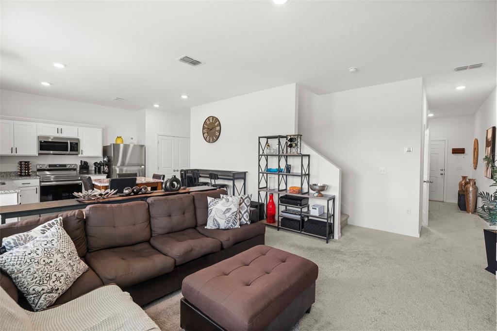 A living room with a brown sectional sofa and ottoman opens to a kitchen area — 8720 SPORTSMAN LOOP, GROVELAND, FL