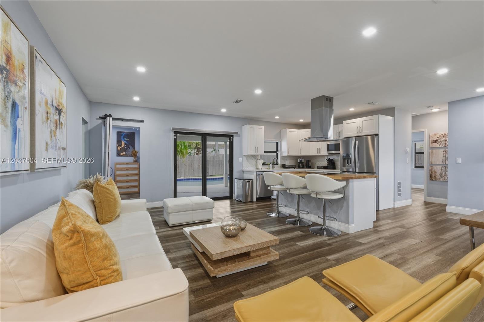 A modern open-concept living room and kitchen featuring white cabinetry, wood flooring, and pool access — 7395 SW 39th St, Miami FL 33155, MIAMI, FL