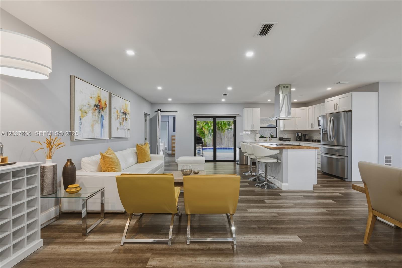 An open-concept living room and kitchen feature white cabinetry, stainless steel appliances, and wood-look flooring — 7395 SW 39th St, Miami FL 33155, MIAMI, FL