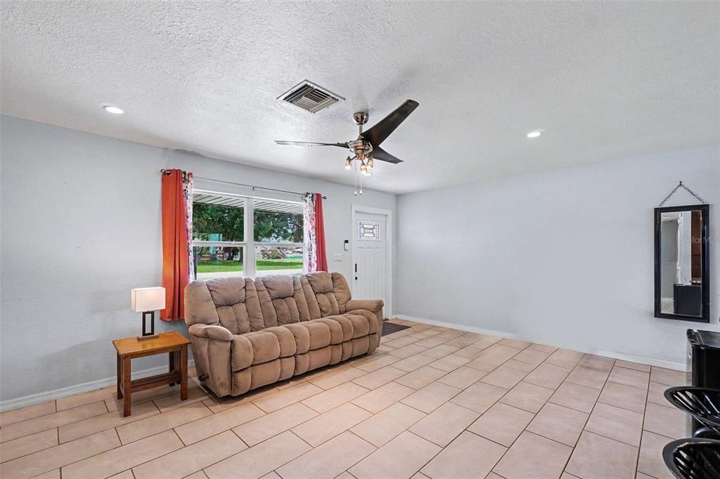 A living room with a beige sofa, tile flooring, a ceiling fan, and a window — 3321 DAUPHINE STREET, SEBRING, FL