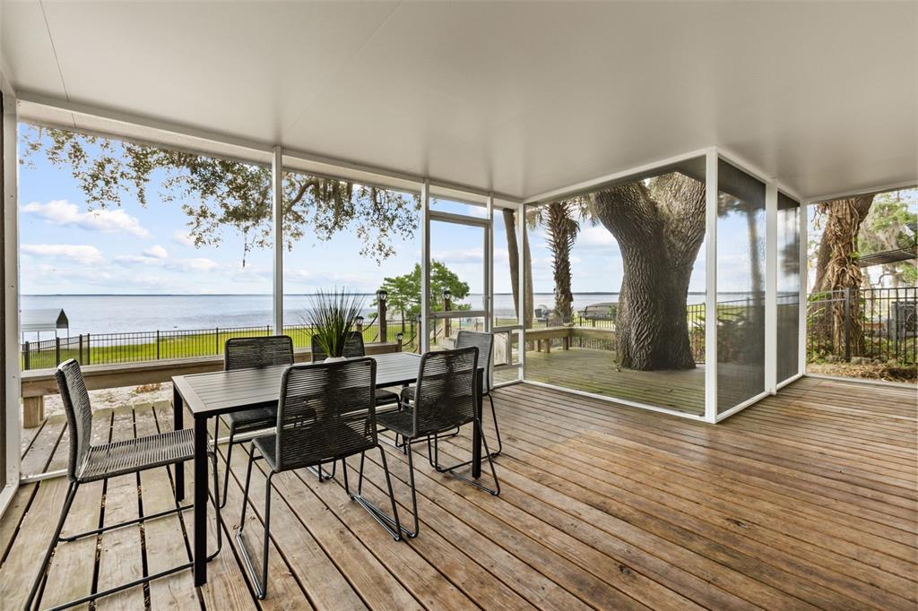 A screened-in wooden deck features a dining set overlooking a lake and large trees — 2462 FORT LANE ROAD, GENEVA, FL