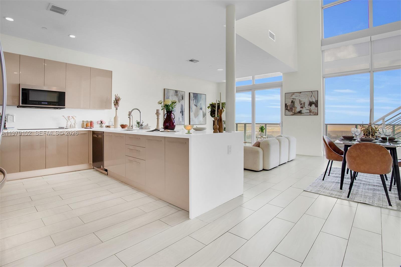 A modern kitchen with beige cabinetry and a white island opens to a dining area — 2000 Metropica Way, Sunrise FL 33323, SUNRISE, FL