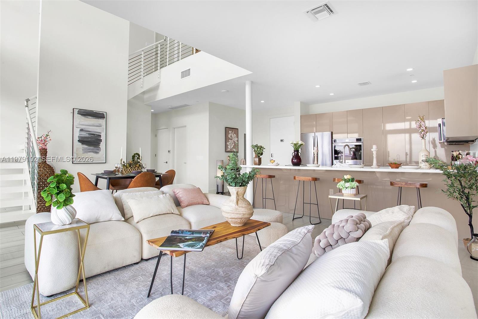 A modern open-concept living room features a white sectional sofa, kitchen island, and staircase — 2000 Metropica Way, Sunrise FL 33323, SUNRISE, FL
