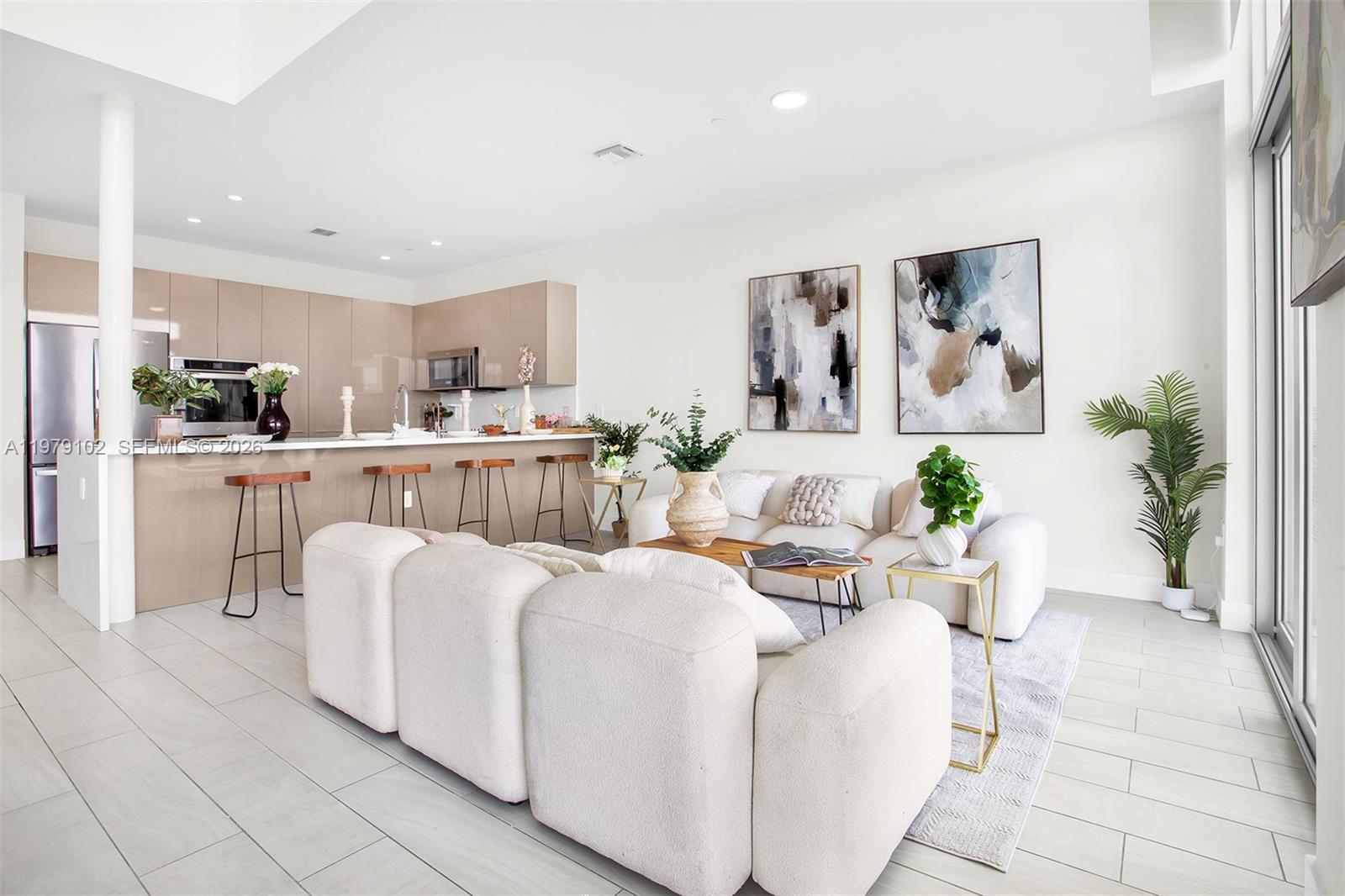 A modern open-concept living room features a kitchen with beige cabinets and a white sofa — 2000 Metropica Way, Sunrise FL 33323, SUNRISE, FL