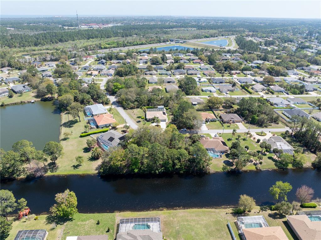 An aerial view shows a suburban neighborhood with houses, swimming pools, and a canal — 37 LUDLOW LANE W, PALM COAST, FL