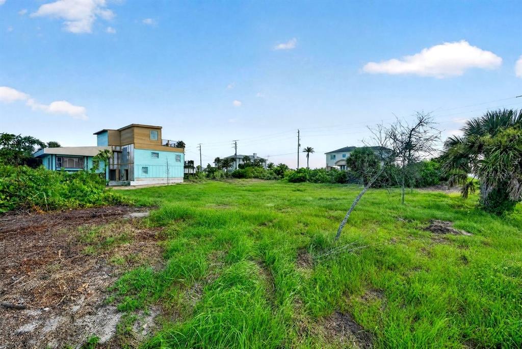 A grassy vacant lot sits in front of a modern two-story house under a blue sky — 4736 S ATLANTIC AVENUE, PONCE INLET, FL