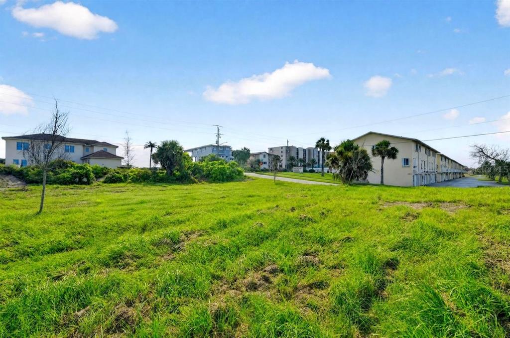A grassy vacant lot sits in front of several multi-story apartment buildings under a blue sky — 4736 S ATLANTIC AVENUE, PONCE INLET, FL