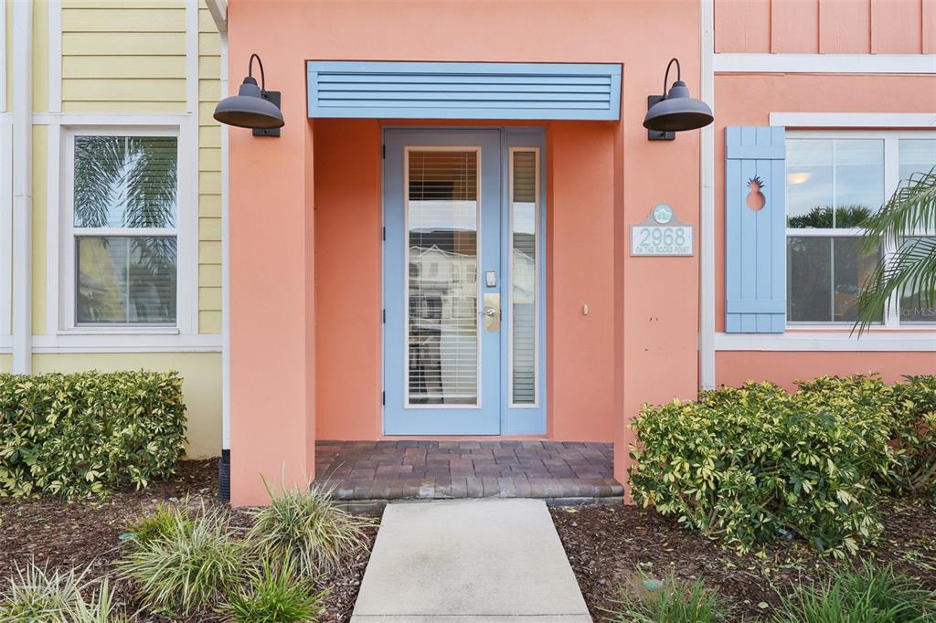 A peach-colored house exterior features a blue front door, two wall-mounted lamps, and landscaping — 2968 ON THE ROCKS POINT, KISSIMMEE, FL