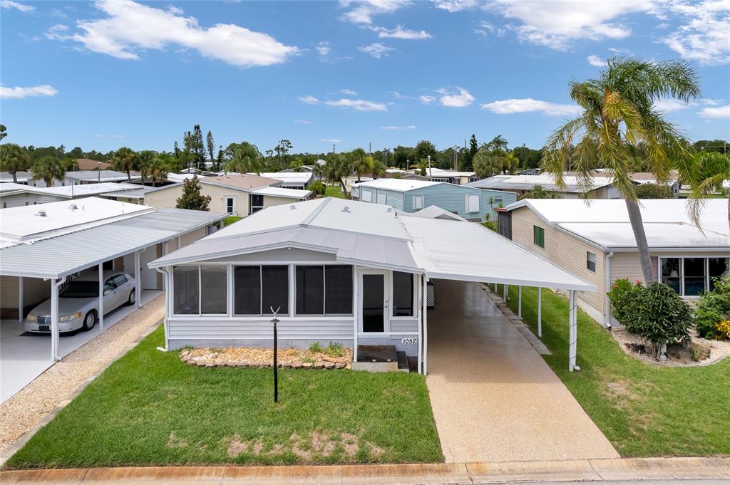 An exterior view of a light gray mobile home with a carport and screened porch — 2100 KINGS HIGHWAY UNIT 1052, PORT CHARLOTTE, FL