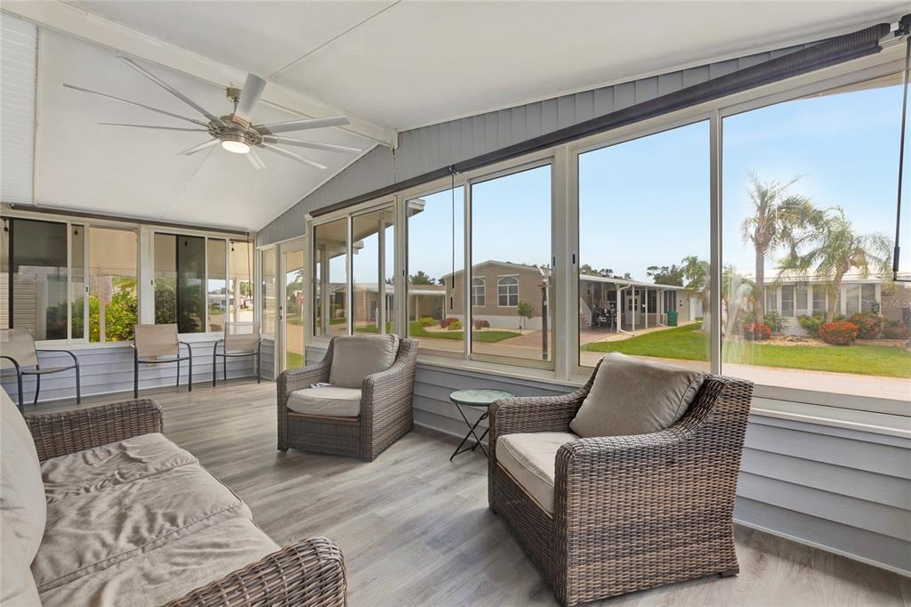 A sunroom features wicker furniture, wood-look flooring, a ceiling fan, and large windows overlooking homes — 2100 KINGS HIGHWAY UNIT 1052, PORT CHARLOTTE, FL