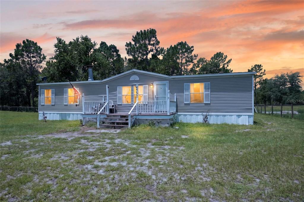 A single-story manufactured home with gray siding and a front deck sits on a lawn — 5730 SE 120TH AVENUE, MORRISTON, FL