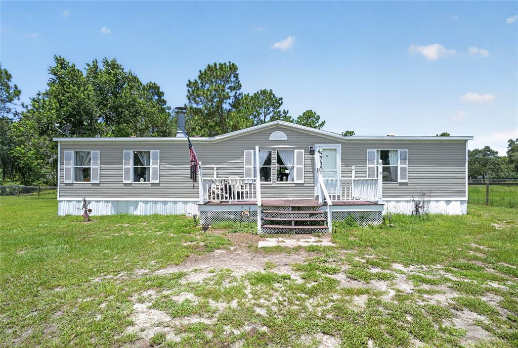 A single-story manufactured home with grey siding and a front deck sits on a grassy lot — 5730 SE 120TH AVENUE, MORRISTON, FL