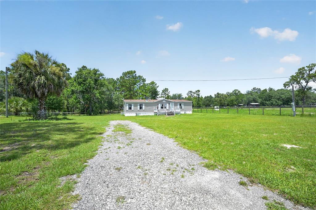 A single-story manufactured home sits at the end of a gravel driveway on a lot — 5730 SE 120TH AVENUE, MORRISTON, FL