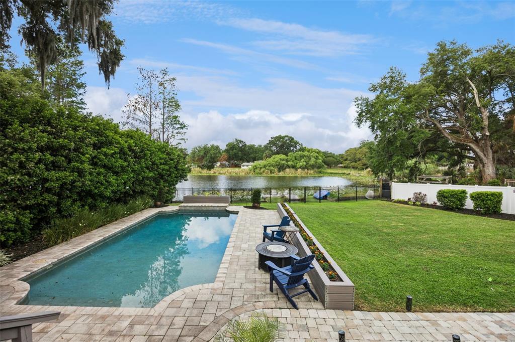 A backyard features a rectangular swimming pool, a paver patio, and a lawn overlooking a lake — 2100 MAE STREET, ORLANDO, FL