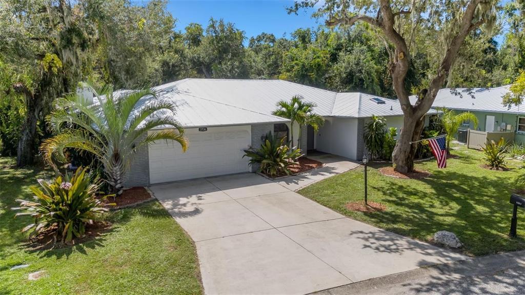 A single-story house with a white metal roof, gray brick facade, and a concrete driveway — 3736 MAPLE HOLLOW COURT, SARASOTA, FL