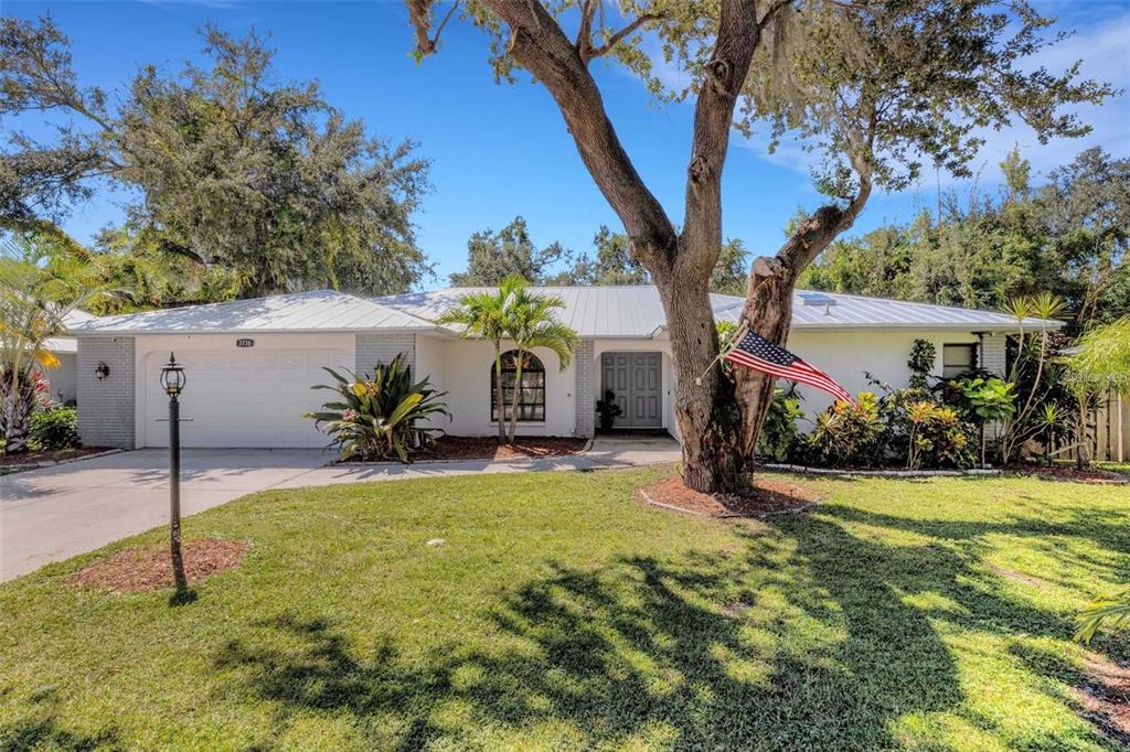 A single-story house with a white exterior, metal roof, and a large tree in front — 3736 MAPLE HOLLOW COURT, SARASOTA, FL
