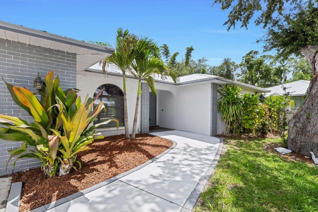A white and gray brick house exterior features a curved walkway and tropical landscaping — 3736 MAPLE HOLLOW COURT, SARASOTA, FL