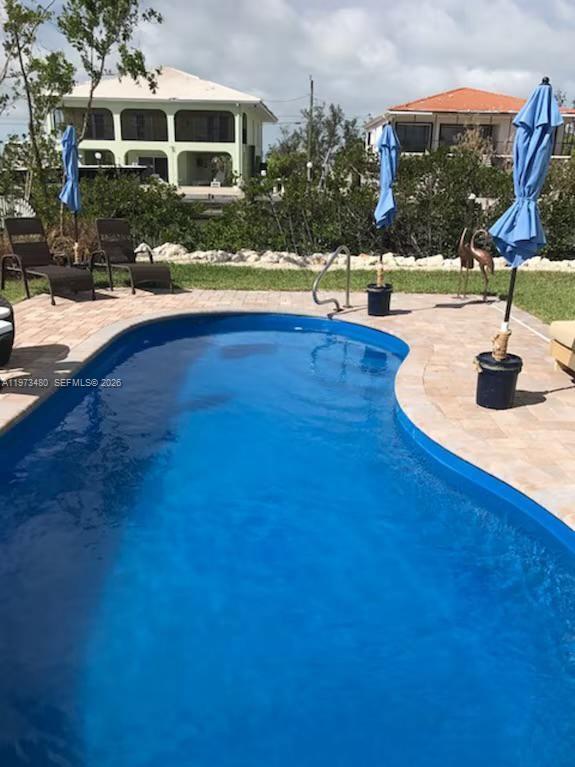 A kidney-shaped swimming pool with a paver deck, lounge chairs, and blue umbrellas — 227 Sombrero Beach Rd, Marathon FL 33050, MARATHON, FL
