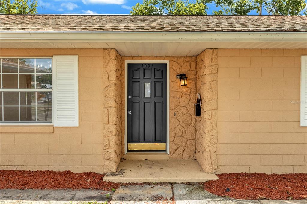A front exterior view of a house featuring a black door and stone-textured siding — 4992 E WIND STREET, ORLANDO, FL