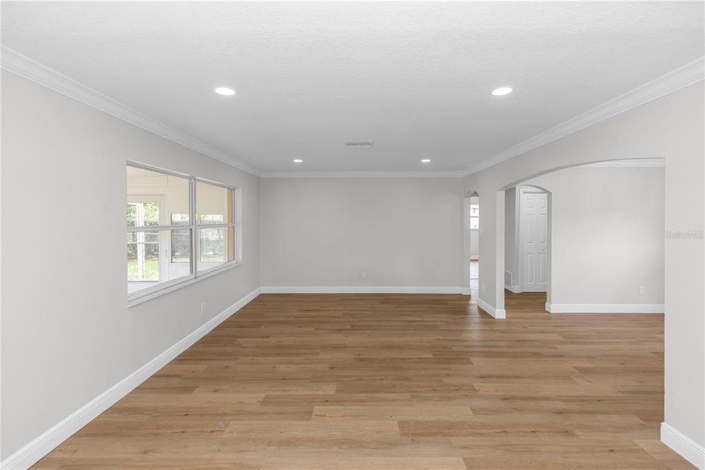 An empty room with light wood-look flooring, white walls, recessed lighting, and an arched doorway — 4992 E WIND STREET, ORLANDO, FL