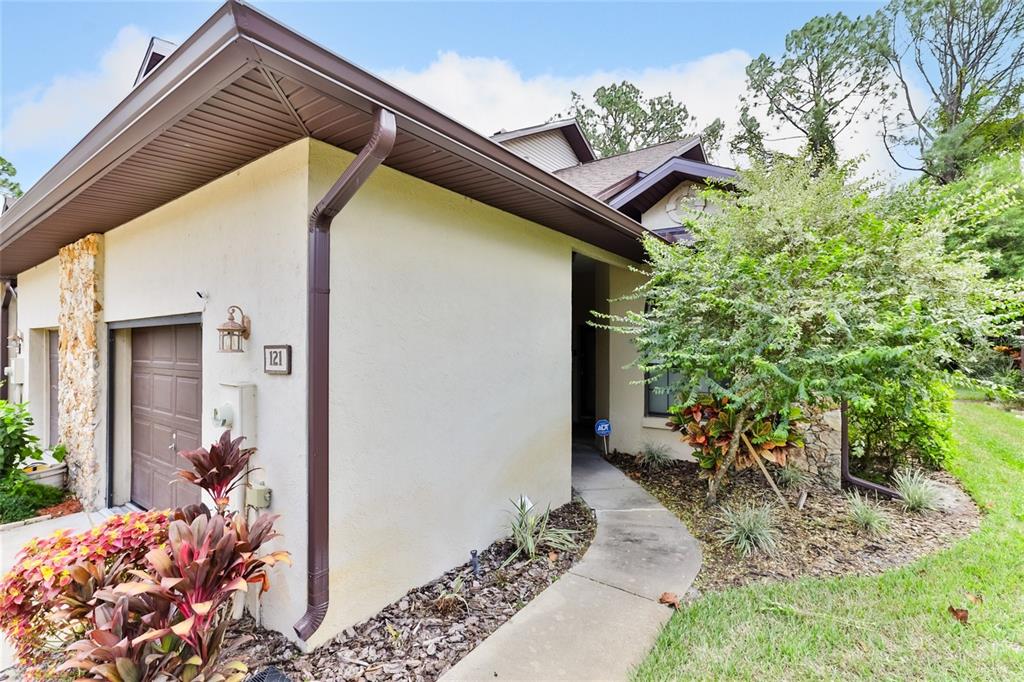A tan stucco house exterior features a brown garage door, stone accents, and a walkway — 121 DOVECOTE LANE, DAYTONA BEACH, FL