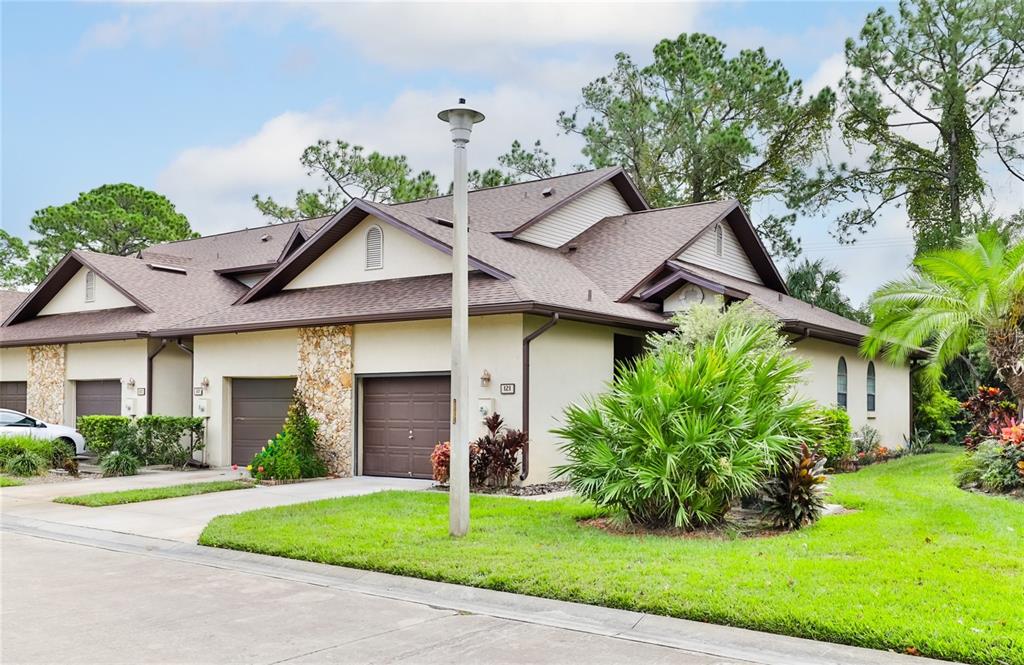 A multi-unit residential building with brown garage doors, stone accents, and a grassy lawn — 121 DOVECOTE LANE, DAYTONA BEACH, FL