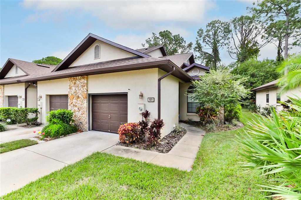 A single-story townhouse with a brown garage door, stone accents, and a concrete walkway — 121 DOVECOTE LANE, DAYTONA BEACH, FL