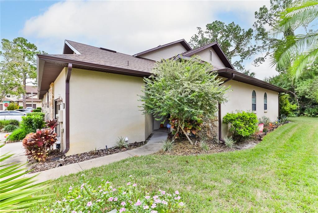 The exterior of a single-story house features a tan stucco facade, stone accents, and landscaping — 121 DOVECOTE LANE, DAYTONA BEACH, FL