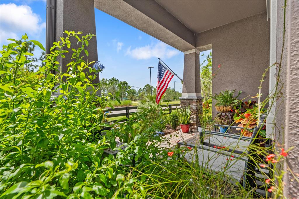 A covered front porch features potted plants, seating, and an American flag on a pole — 11874 BLAMEY TRAIL, ODESSA, FL