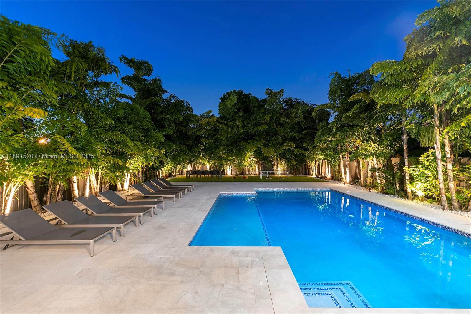 A rectangular swimming pool is surrounded by lounge chairs and lush trees at night — 6529 SW 30th St, Miami FL 33155, MIAMI, FL