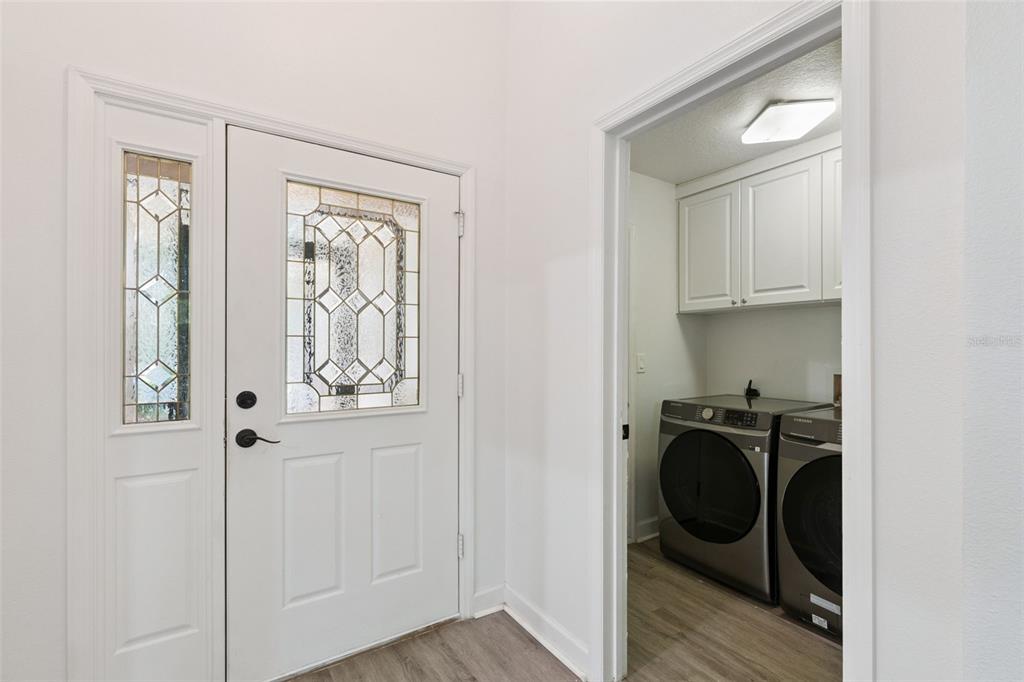 A white front door with decorative glass panels sits beside a laundry room with appliances — 3022 NEW HAVEN PLACE, MOUNT DORA, FL
