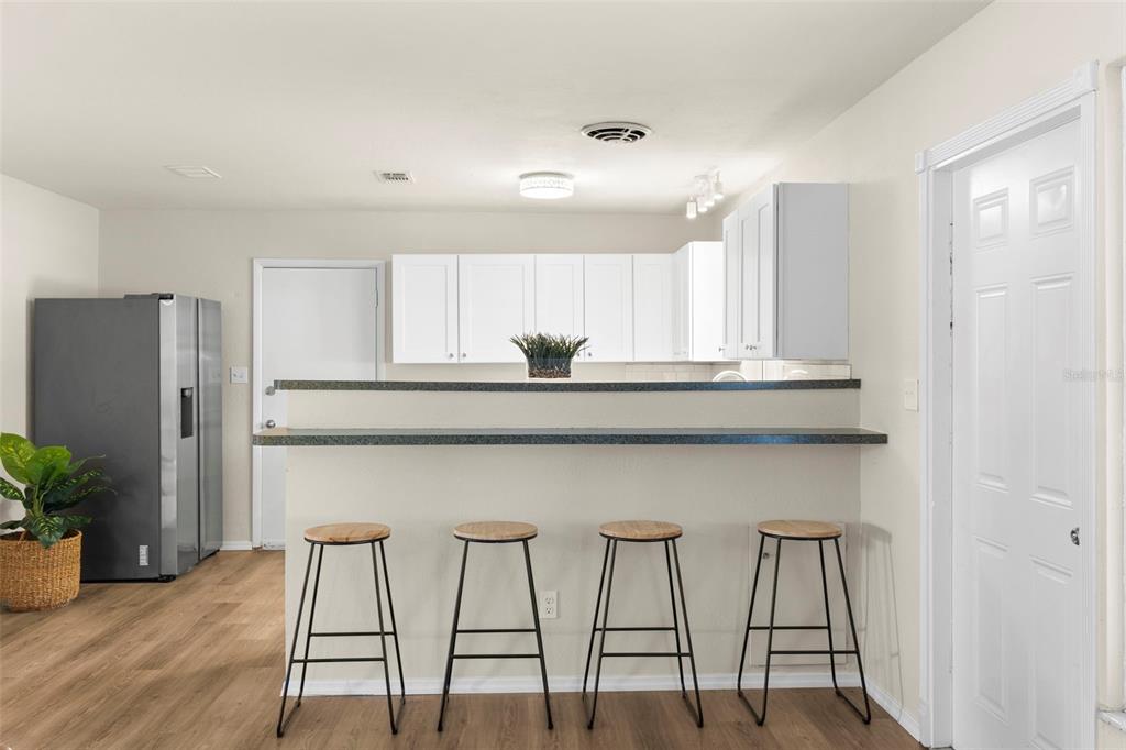 A kitchen features white cabinets, a breakfast bar with four stools, and wood-look flooring — 7420 DR MARTIN LUTHER KING JR STREET N, ST PETERSBURG, FL