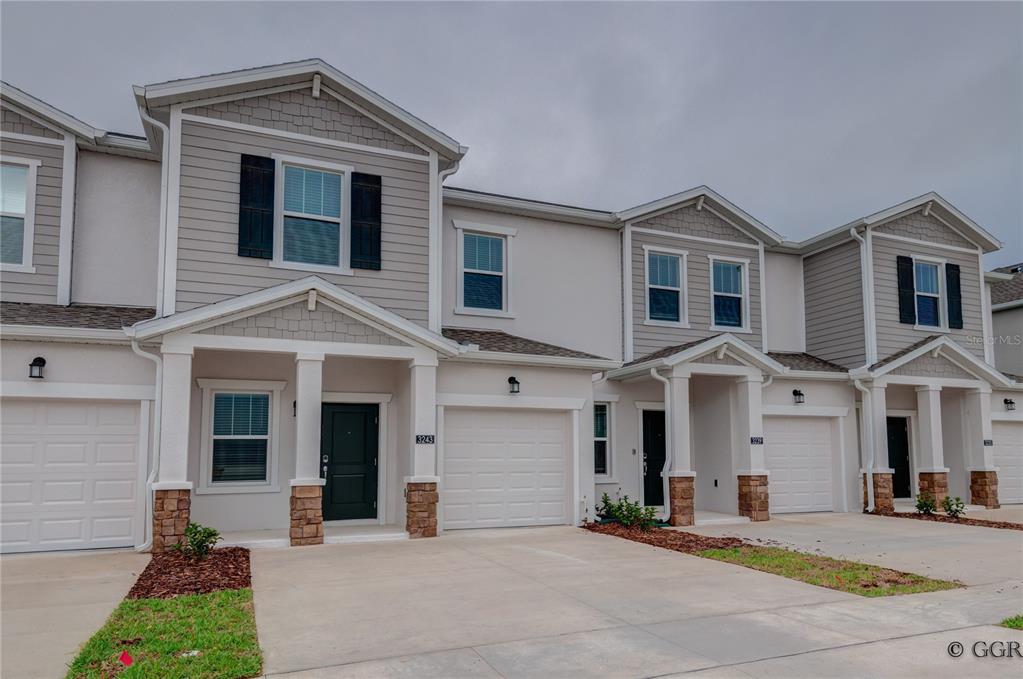 A row of modern two-story townhomes with light-colored siding, stone accents, and attached garages — 3243 LAURENT LOOP, DAVENPORT, FL