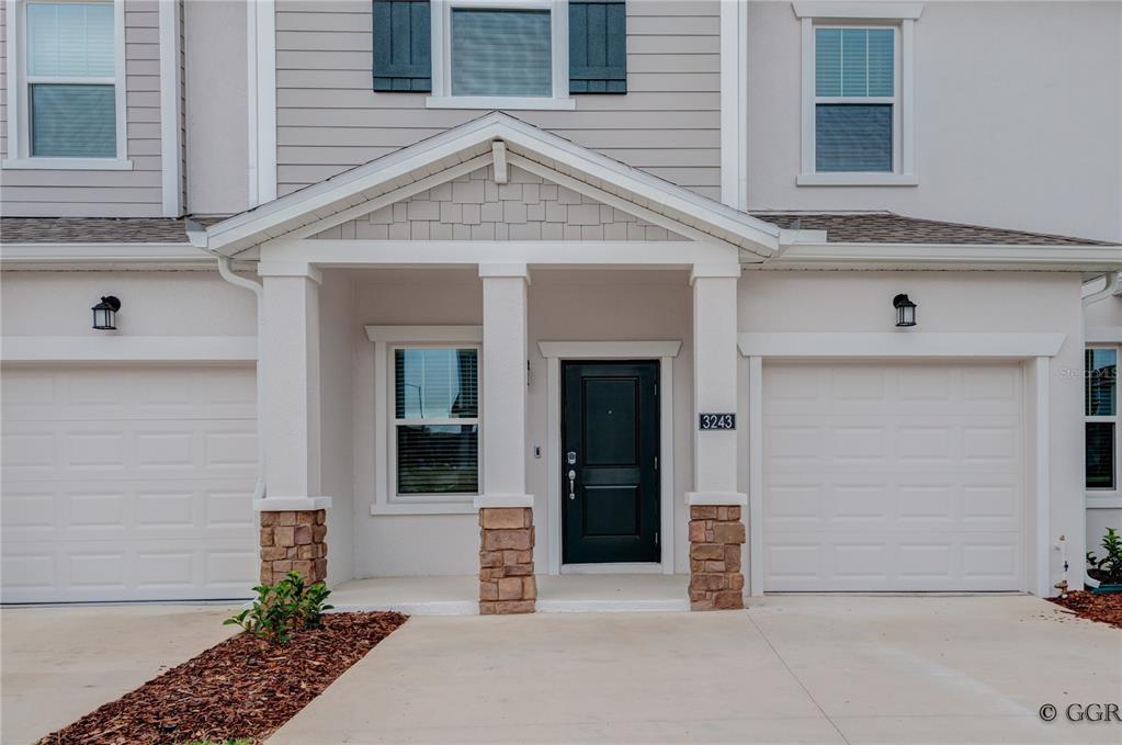 The exterior of a two-story townhouse features a covered entryway, stone pillars, and two garages — 3243 LAURENT LOOP, DAVENPORT, FL