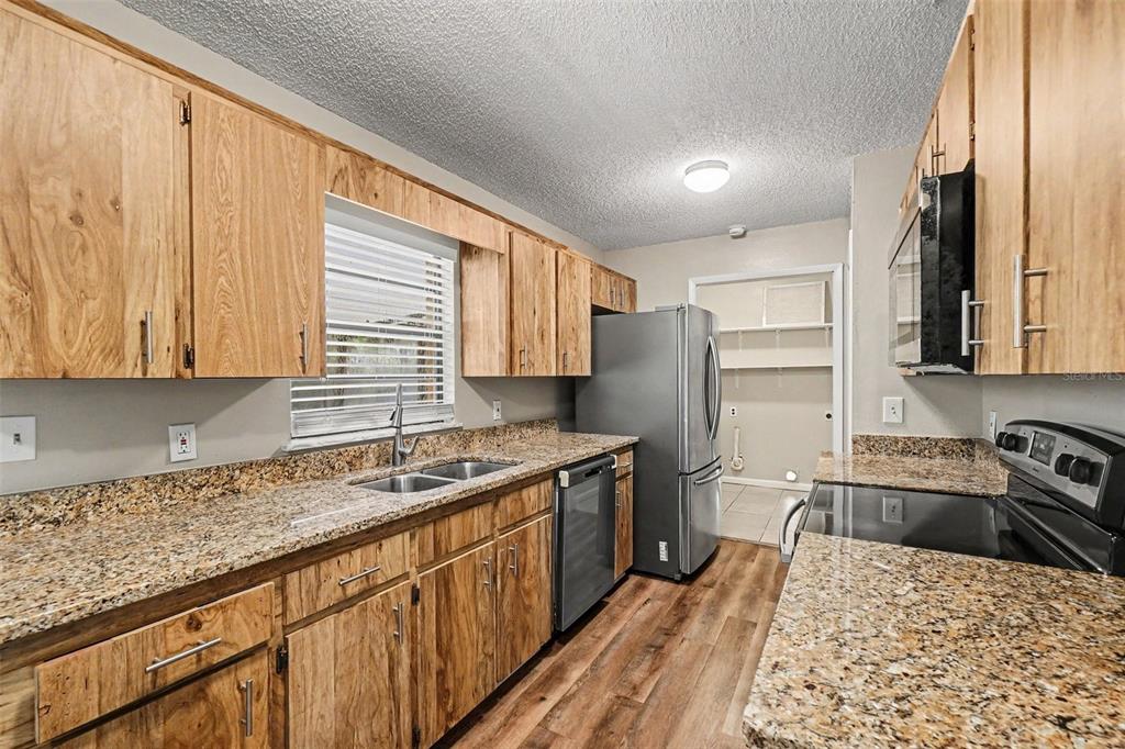 A kitchen features wood cabinets, granite countertops, stainless steel appliances, and wood-look flooring — 2345 NORTHVIEW DRIVE, LAKELAND, FL