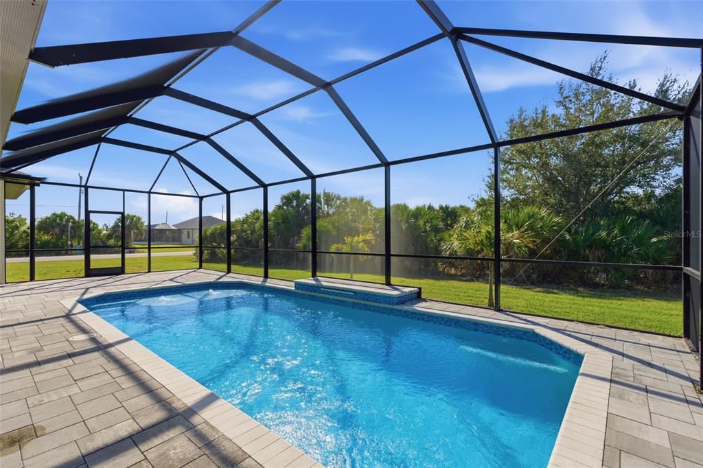 A rectangular swimming pool sits inside a screened-in patio with light-colored stone pavers — 14361 FORT MYERS AVENUE, PORT CHARLOTTE, FL