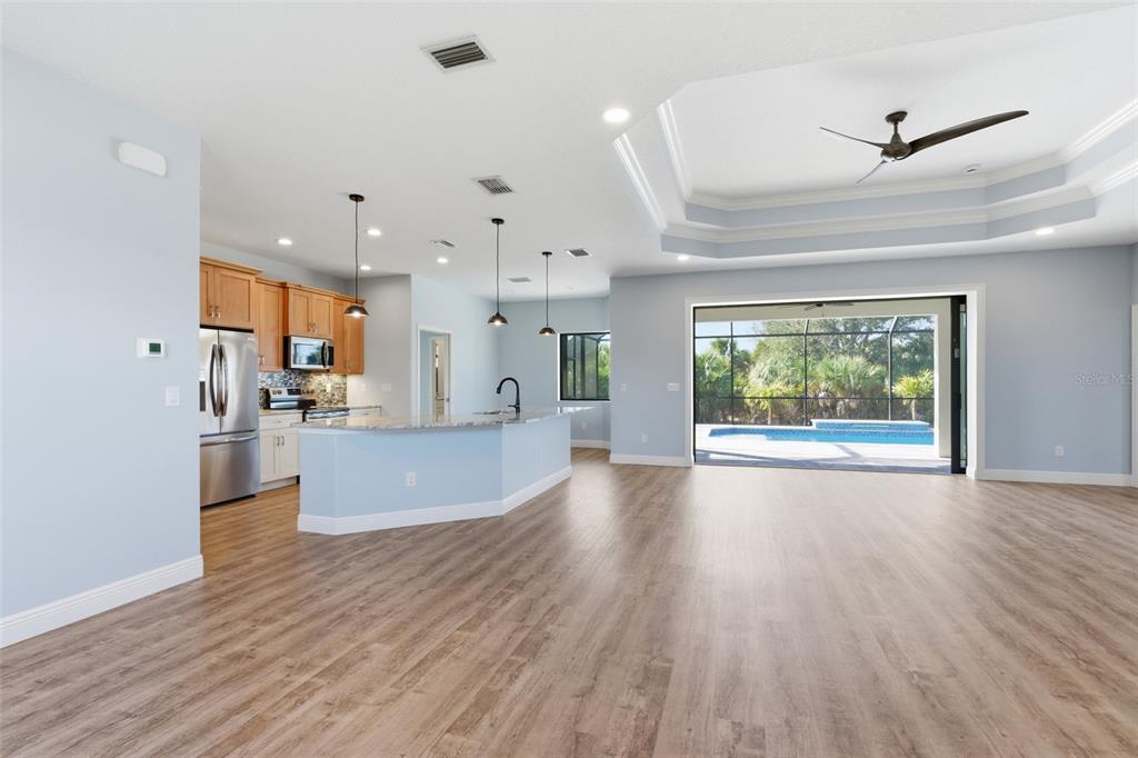 An open-concept kitchen and living area with light blue walls, wood flooring, and pool access — 14361 FORT MYERS AVENUE, PORT CHARLOTTE, FL