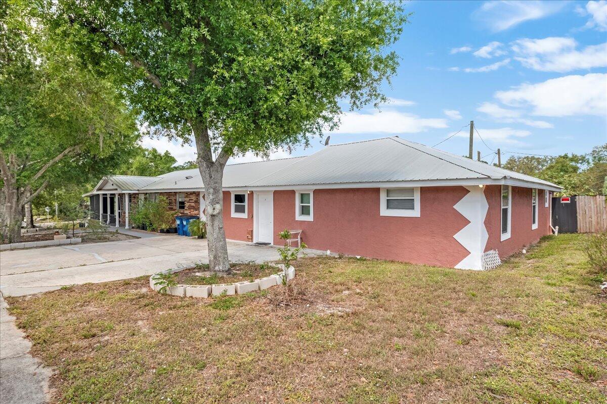 A single-story house with a red stucco exterior, a metal roof, and a large tree — 216 Micco Avenue, Sebring FL 33870, SEBRING, FL
