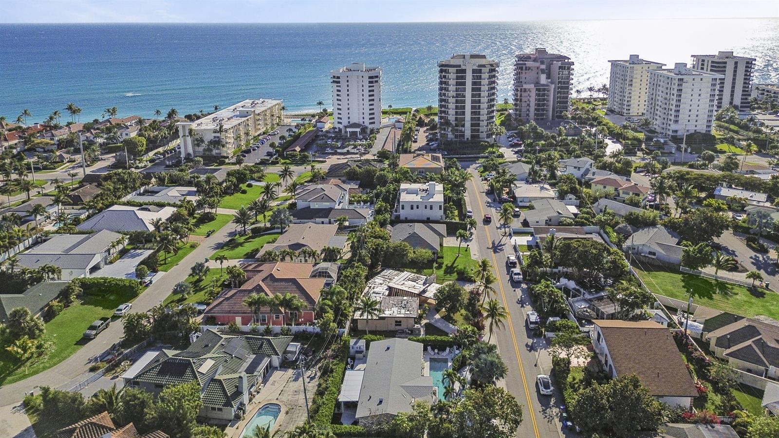 An aerial view shows a coastal neighborhood with residential homes, palm trees, and high-rise buildings — 471 Mars Way, Juno Beach FL 33408, JUNO BEACH, FL