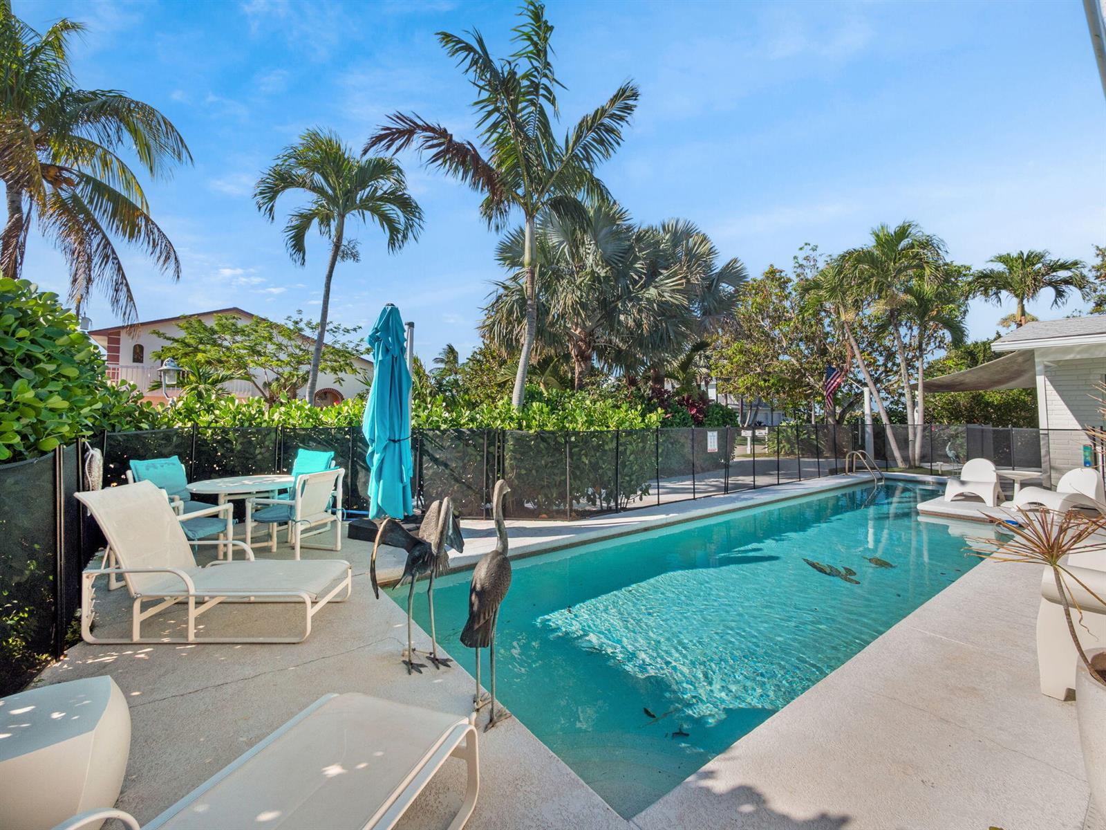 A swimming pool with lounge chairs and palm trees in a fenced backyard — 471 Mars Way, Juno Beach FL 33408, JUNO BEACH, FL