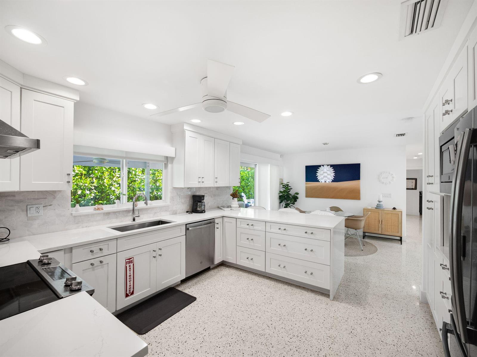 A bright kitchen features white cabinetry, quartz countertops, stainless steel appliances, and terrazzo flooring — 471 Mars Way, Juno Beach FL 33408, JUNO BEACH, FL