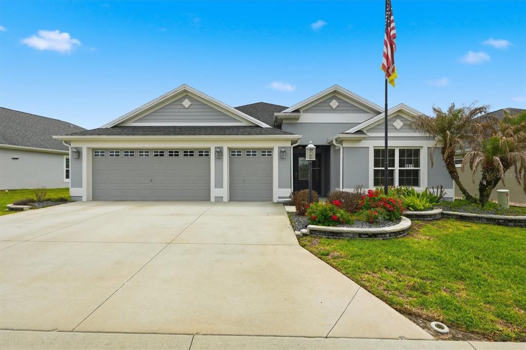 A single-story house with a gray exterior, a three-car garage, and an American flag — 5819 WHITE IBIS RUN, THE VILLAGES, FL